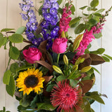 Bouquet of flowers including sunflowers, roses, and proteas against a light background