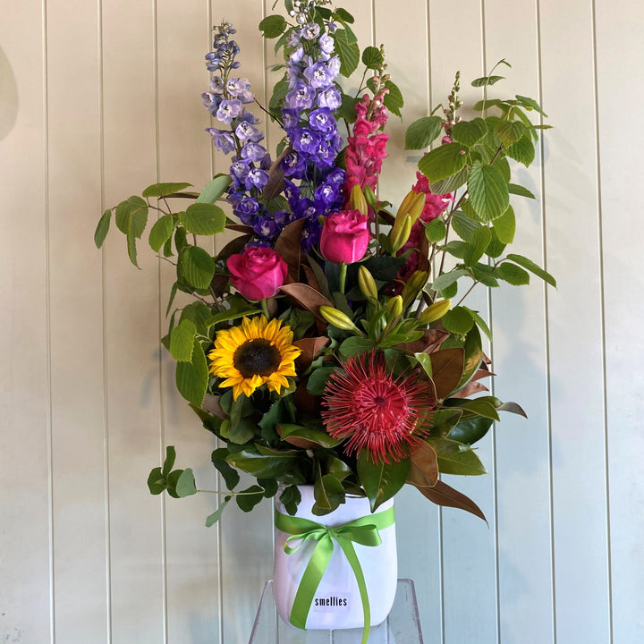 Bouquet of colorful flowers in a white vase with a green ribbon against a wooden panel background.