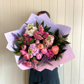 Person holding a large bouquet of flowers against a light wooden panel background