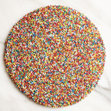 Round chocolate covered in multicolored sprinkles on a marble surface