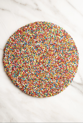 Round chocolate covered in multicolored sprinkles on a marble surface