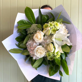 Bouquet of flowers wrapped in paper held by a person against a light wooden panel background