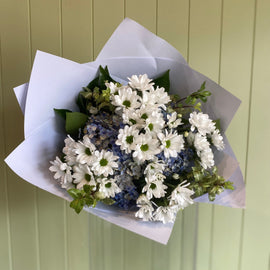 Bouquet of white and blue flowers wrapped in paper against a green wooden background