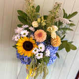 Bouquet of flowers with sunflower, daisies, and hydrangeas against a white wooden background