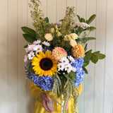 Person holding a colorful bouquet of flowers against a white wall.