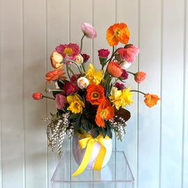 Colorful flower arrangement in a clear vase against a light wooden panel background