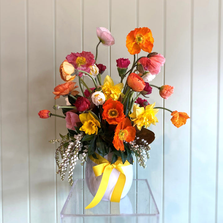 Colorful flower arrangement in a clear vase against a light wooden panel background