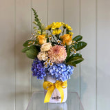 Bouquet of flowers with a yellow ribbon on a glass table against a white paneled wall.