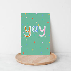 Hand drawn letters that spell out YAY on a green background and colorful confetti sprinkled all around,