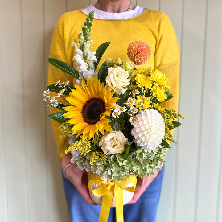 Person holding a bouquet of sunflowers and other flowers against a white wall.