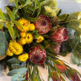 Bouquet of flowers with yellow and red proteas, greenery, and other assorted flowers.