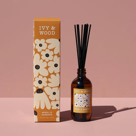 Brown diffuser bottle with black sticks and decorative box labeled 'Ivy & Wood' on a pink background