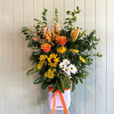 Bouquet of flowers with a white container and orange ribbon against a light wooden panel background
