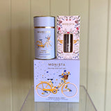 Monista tea packaging including a canister, box, and tea infuser on a wooden surface.