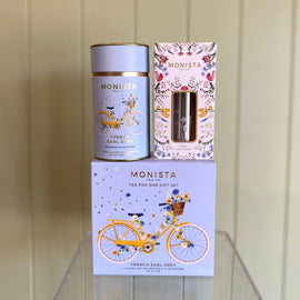 Monista tea packaging including a canister, box, and tea infuser on a wooden surface.