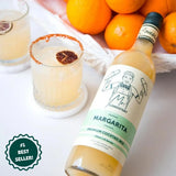 Bottle of margarita mix with glasses and oranges on a white surface