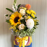 Bouquet of flowers with sunflowers and a yellow ribbon held by a person wearing blue pants.