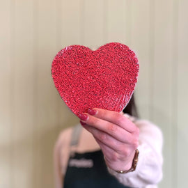 Hand holding a red glittery heart-shaped object against a neutral background