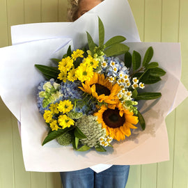 Person holding a bouquet of flowers wrapped in white paper against a green wall.