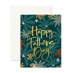 The Smellies Flowers HAPPY FATHER'S DAY GREETING CARD features "Happy Father's Day" in gold script on a dark green, tropical leaf background with small flowers. Includes an off-white envelope—perfect for sending special wishes to dad.